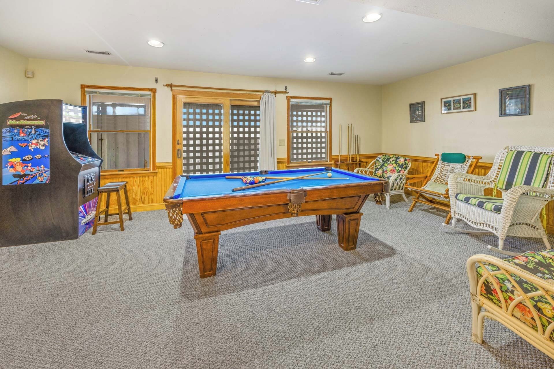 A pool table in a room with a carpeted floor, wooden chairs, and a pool table.