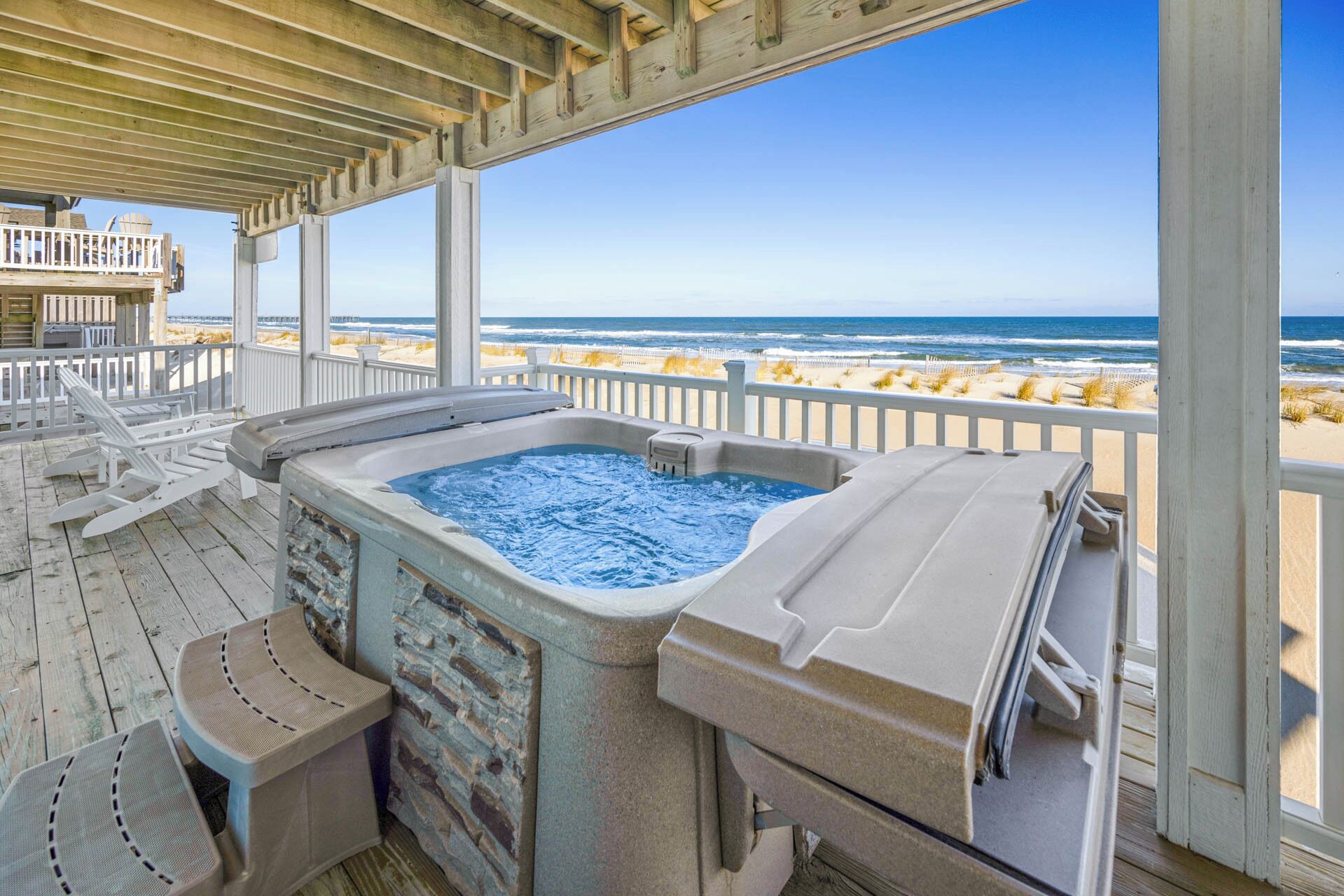 Ein Whirlpool auf einer Holzterrasse mit Blick auf Strand und Meer.