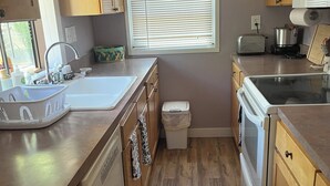 Une cuisine avec des meubles de rangement en bois, un évier, une cuisinière et une fenêtre avec des stores.