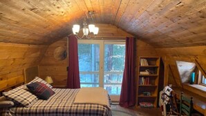 A cozy attic bedroom with a large bed, a bookshelf, and a window with curtains.