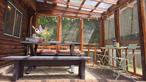 A wooden cabin with a covered porch, a picnic table, and a bench.