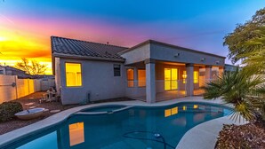 Ein modernes Haus mit Swimmingpool, einer überdachten Terrasse und Blick auf den Sonnenuntergang.