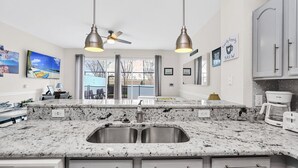 A modern kitchen with a granite countertop, stainless steel sink, and overhead lighting. - Disney | Townhouse | Pool | Windsor Hills (Kissimmee)