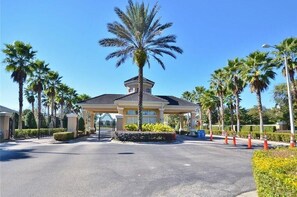 A gated entrance with a palm tree, surrounded by palm trees and a clear sky.