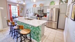 Een moderne keuken met een centraal eiland, barkrukken, roestvrijstalen apparatuur en decoratieve borden aan de muur.
