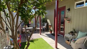 A covered patio area with artificial grass, outdoor furniture, and potted plants.