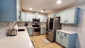 A modern kitchen with light blue cabinets, stainless steel appliances, and a marble backsplash.