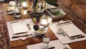 A dining table set for four with a vase of flowers, candles, and a fireplace in the background.