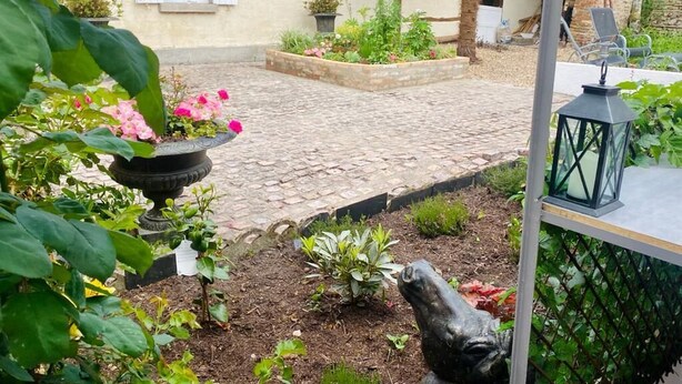 A courtyard with a cobblestone path, a statue, and a house with a tiled roof.