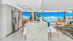 Een moderne keuken met een marmeren kookeiland, roestvrijstalen apparatuur en een balkon met uitzicht op de oceaan.