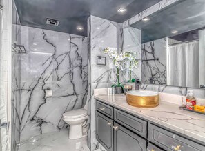 A bathroom with a marble wall, a toilet, a sink with a gold basin, and a mirror. - One-of-a-Kind Oceanfront, Designer Furnished, Luxury Condo w/ Resort Amenities (Myrtle Beach)