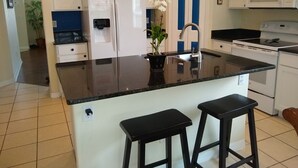Una cocina con una isla central, armarios blancos, un lavamanos de acero inoxidable y un microondas.
