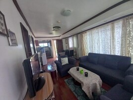 Una sala de estar con sofá, una mesa de centro, televisión y una cocina al fondo.