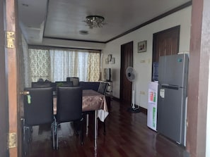 A dining area with a table and chairs, a refrigerator, a fan, and a door leading to another room. - Cozy City Condo/apartment Escape in Davao (Davao)