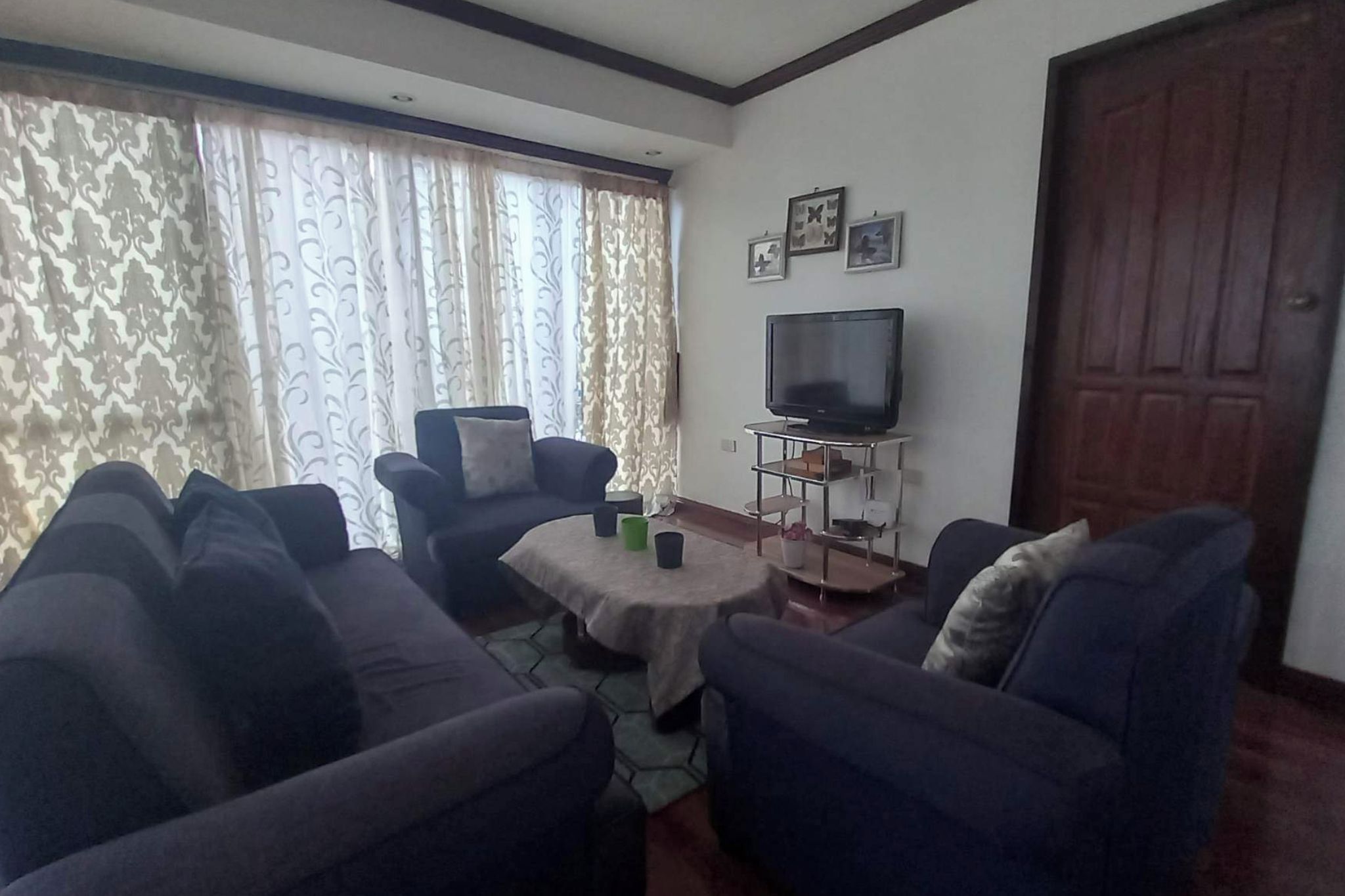 A living room with a sofa set, a coffee table, a TV on a stand, and a door.