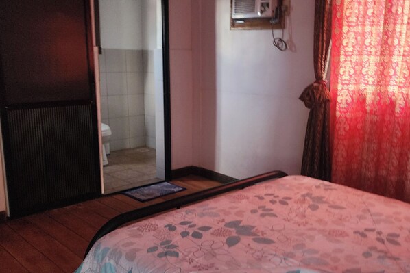 Un dormitorio con cama, puerta corredera hacia un baño y ventana con cortinas.