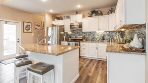 A modern kitchen with white cabinets, granite countertops, and a central island with stools. - Martinis & Bikinis, a beach front house with toes in the sand drink in the hand. (Freeport)