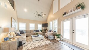 A spacious living room with a high ceiling, a ceiling fan, and a large sliding glass door leading to a balcony. - Martinis & Bikinis, a beach front house with toes in the sand drink in the hand. (Freeport)