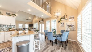 A spacious kitchen with a central island, white cabinetry, and a dining area with blue chairs. - Martinis & Bikinis, a beach front house with toes in the sand drink in the hand. (Freeport)