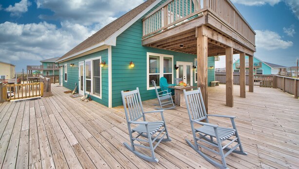 A wooden deck with rocking chairs and a covered area with a railing. - Martinis & Bikinis, a beach front house with toes in the sand drink in the hand. (Freeport)