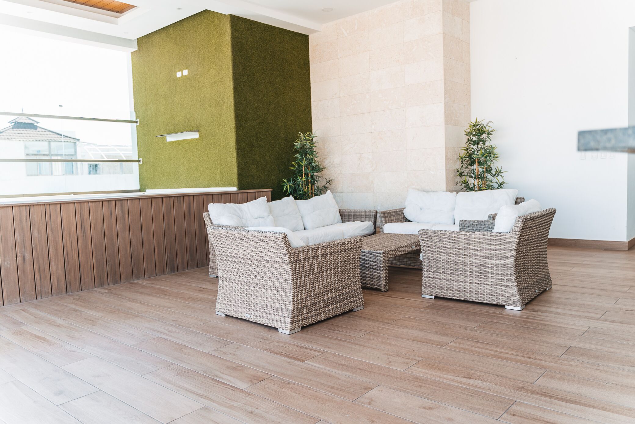 Un espace de détente moderne, avec des meubles en osier, un mur d’accent vert et une vue sur les bâtiments environnants.