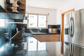 Una cocina moderna con un refrigerador de acero inoxidable, armarios de madera y una encimera negra.