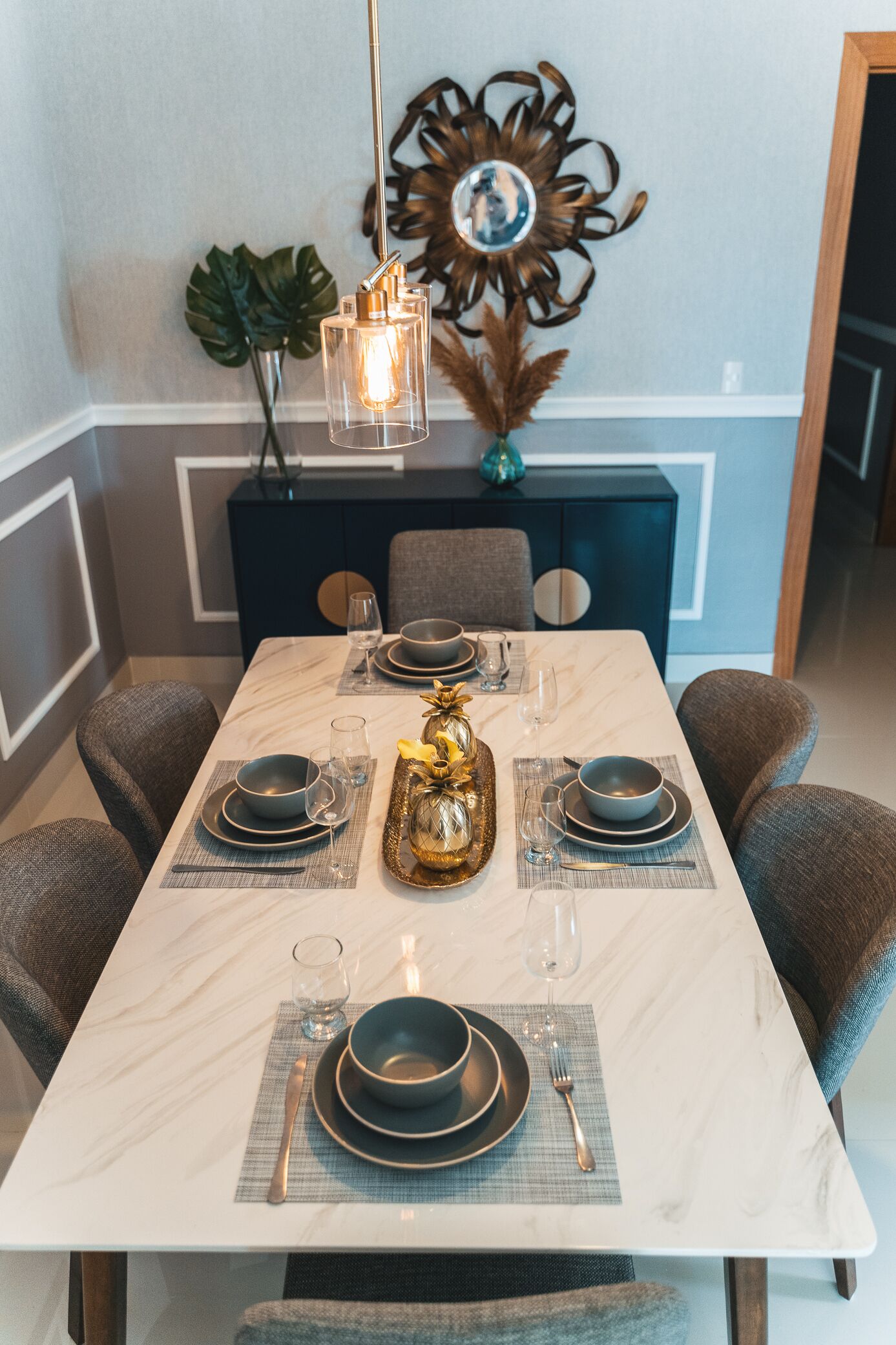 A dining area with a marble table, grey upholstered chairs, and a decorative centerpiece.