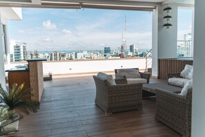 Una terraza en la azotea con mobiliario de mimbre, una pequeña barra y vistas del horizonte de la ciudad.