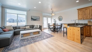 Uma sala de estar moderna com um sofá cinzento, uma mesa de centro e um espaço de jantar com uma ilha de madeira e cadeiras.