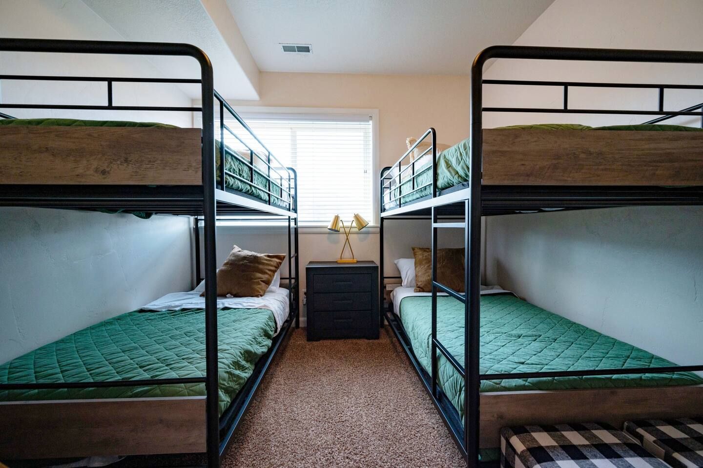 Un dormitorio con literas, un pequeño aparador y una ventana con persianas.