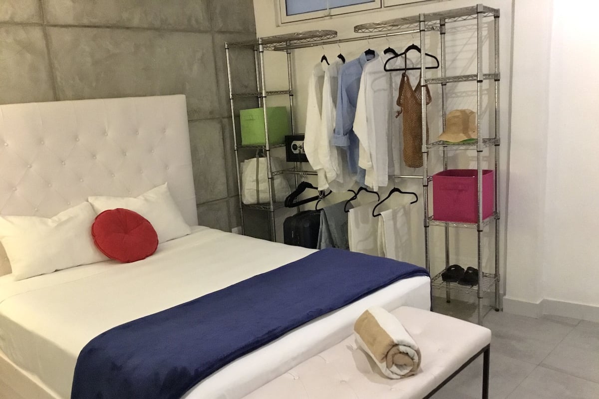 Ein ordentlich bezogenes Bett mit einem weißen Kopfteil, einem roten Kissen und einer blauen Bettdecke.