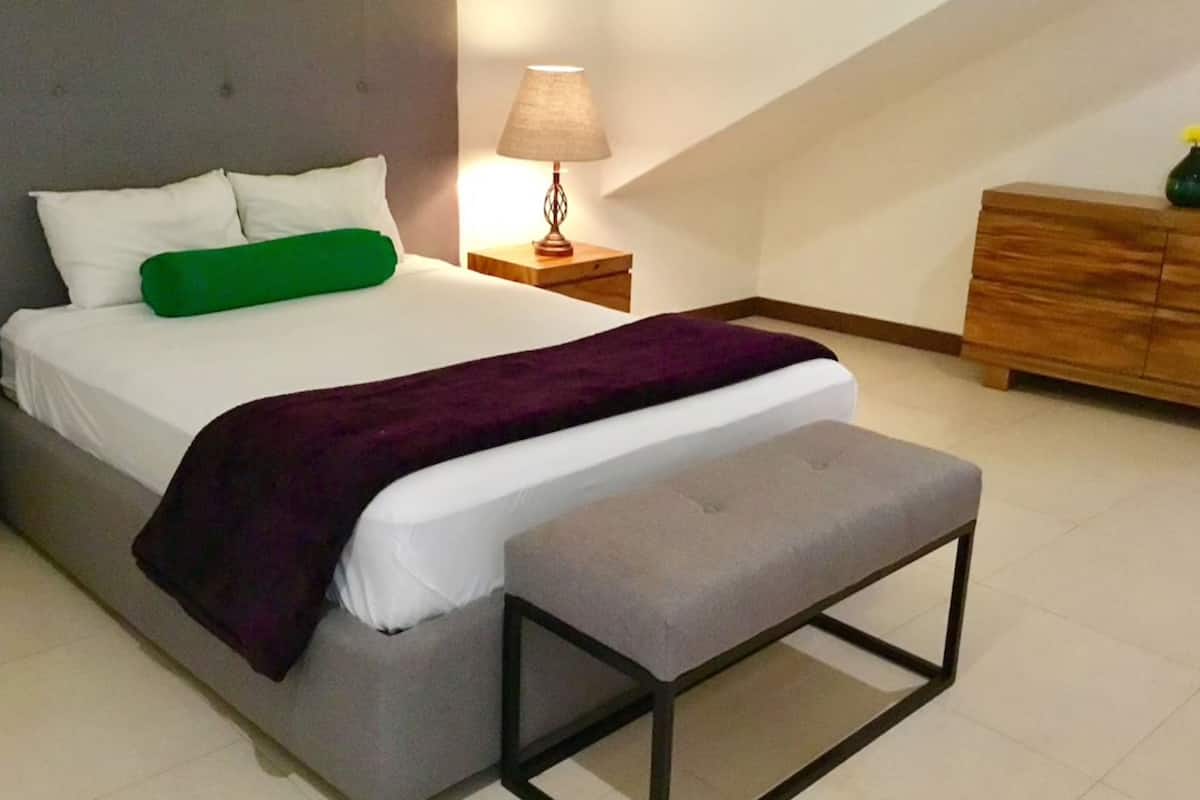 Ein Schlafzimmer mit einem Bett, einem Nachttisch mit Lampe, einer Kommode und einer Bank.
