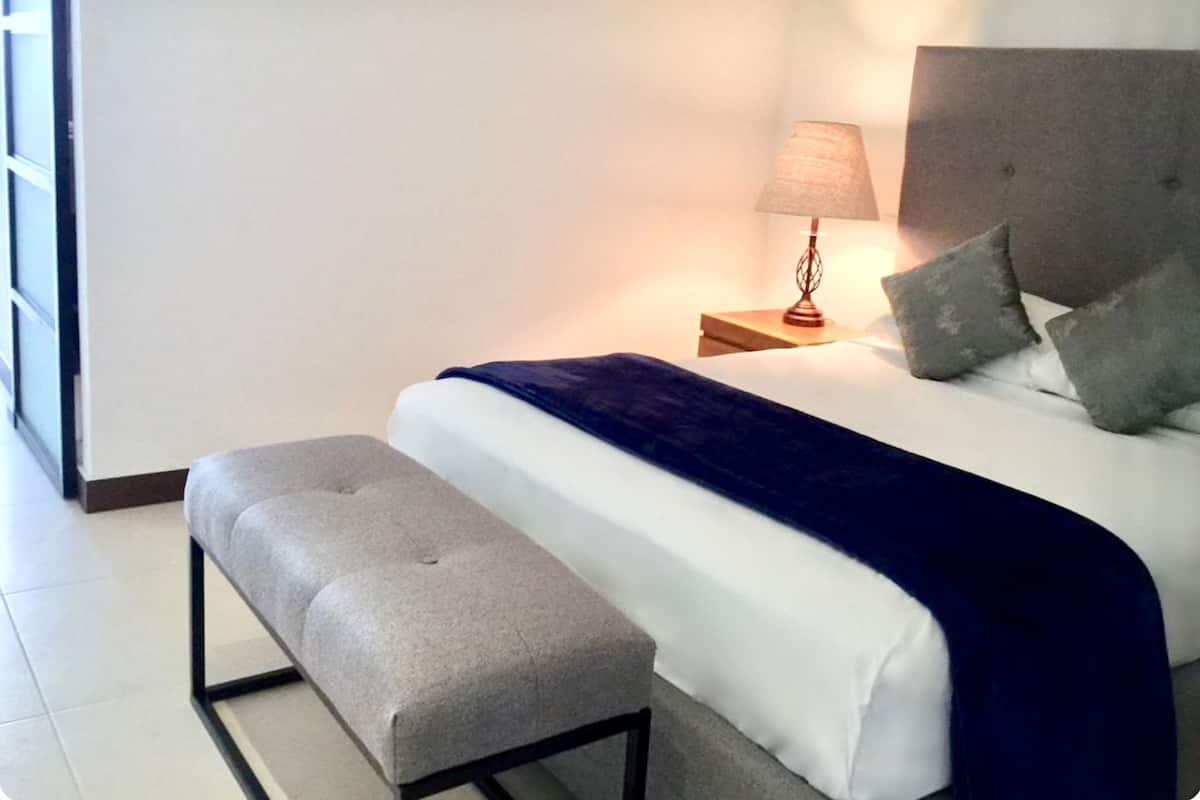 Ein ordentlich gemachtes Bett mit blauer Decke, einer Nachttischlampe und einem kleinen Nachttisch.