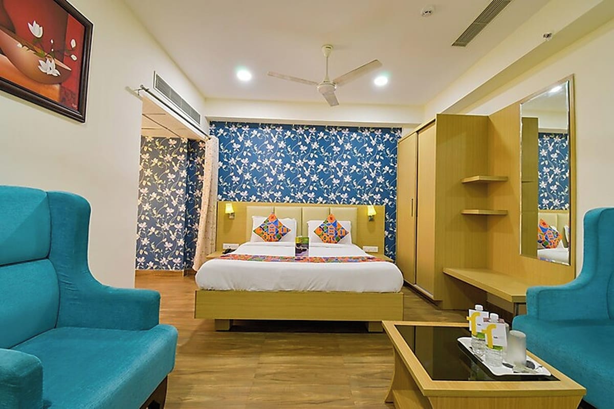 A hotel room with a bed, two armchairs, a bedside table, a ceiling fan, and a large mirror.