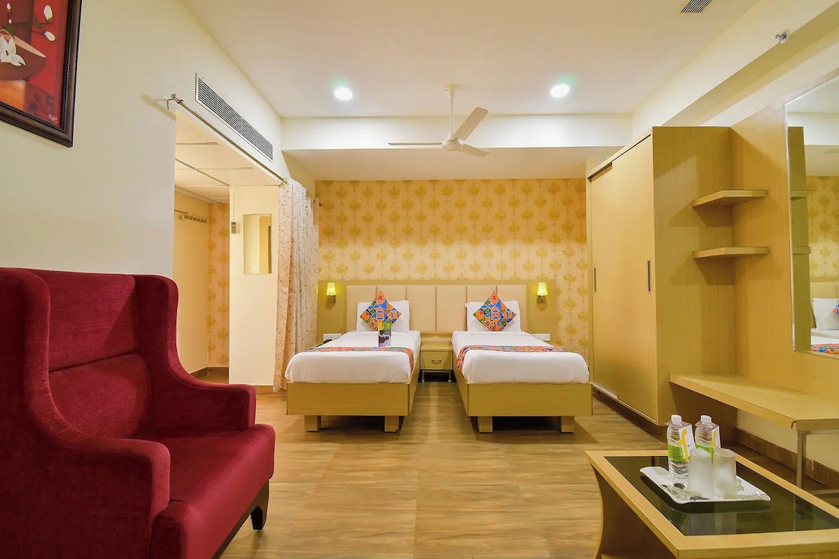 A hotel room with two beds, a red armchair, a small table with water bottles, and a mirror.
