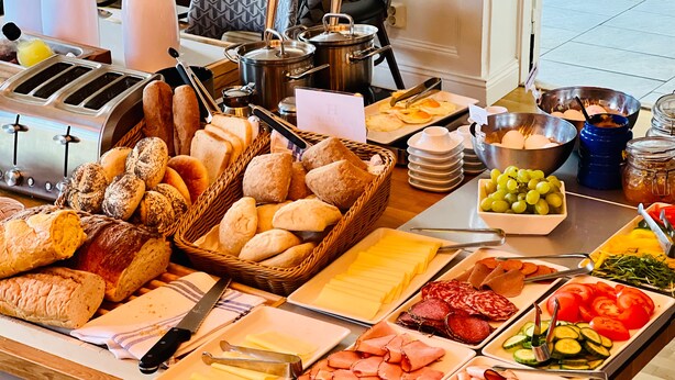 En buffet med forskellige retter, herunder brød, oste, kød og grøntsager.