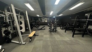 Et fitnessrum med forskellig styrketræningsudstyr, bænk og spejl.