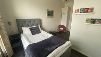 Un dormitorio ordenado con una cama grande, una mesita de noche, una silla, un armario y una estantería con libros.