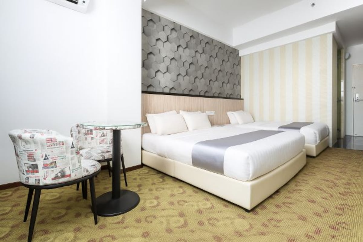 Habitación de hotel con cama, dos mesitas de noche, una silla y alfombra estampada.