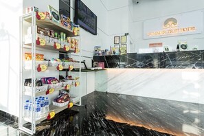A hotel reception area with a marble counter, shelves stocked with snacks and beverages, and a sign for the Summer Tree Hotel.