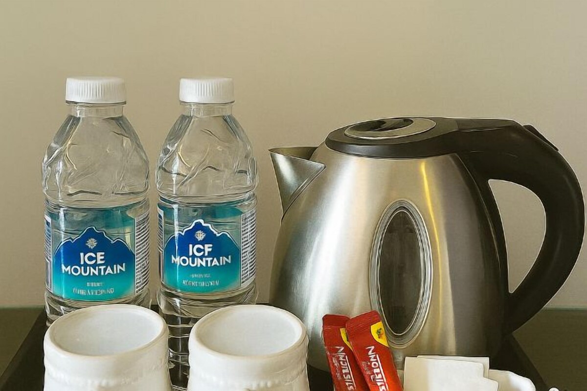 Dos botellas de agua Ice Mountain, un hervidor de acero inoxidable y dos tazas blancas sobre una bandeja.
