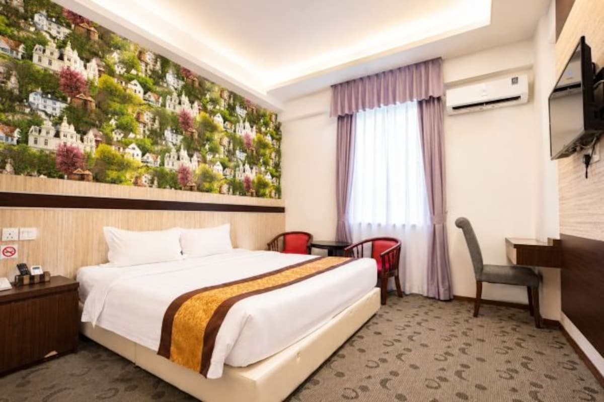 Habitación de hotel con cama, escritorio, silla, televisor montado en la pared y ventana con cortinas.