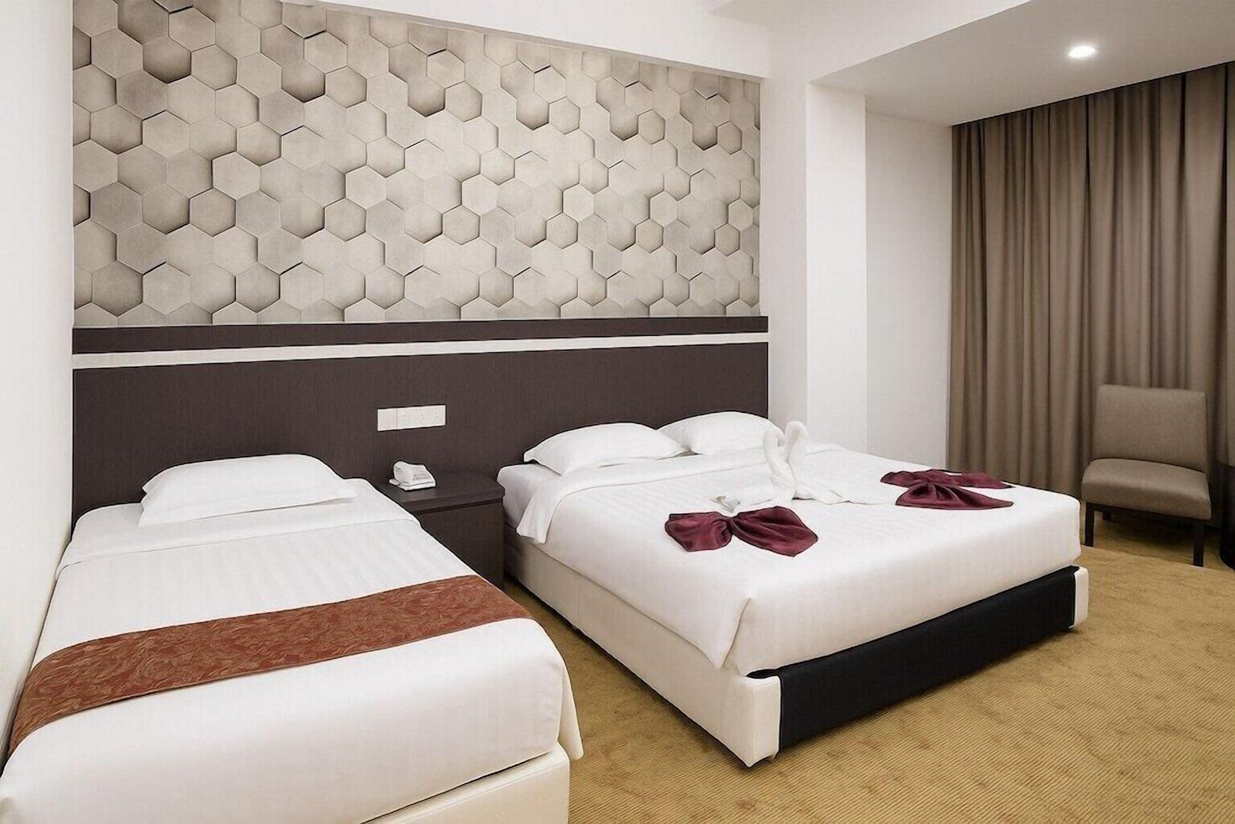 Two beds with white linens, a brown throw, a headboard with a hexagonal pattern, a chair, and a curtain.