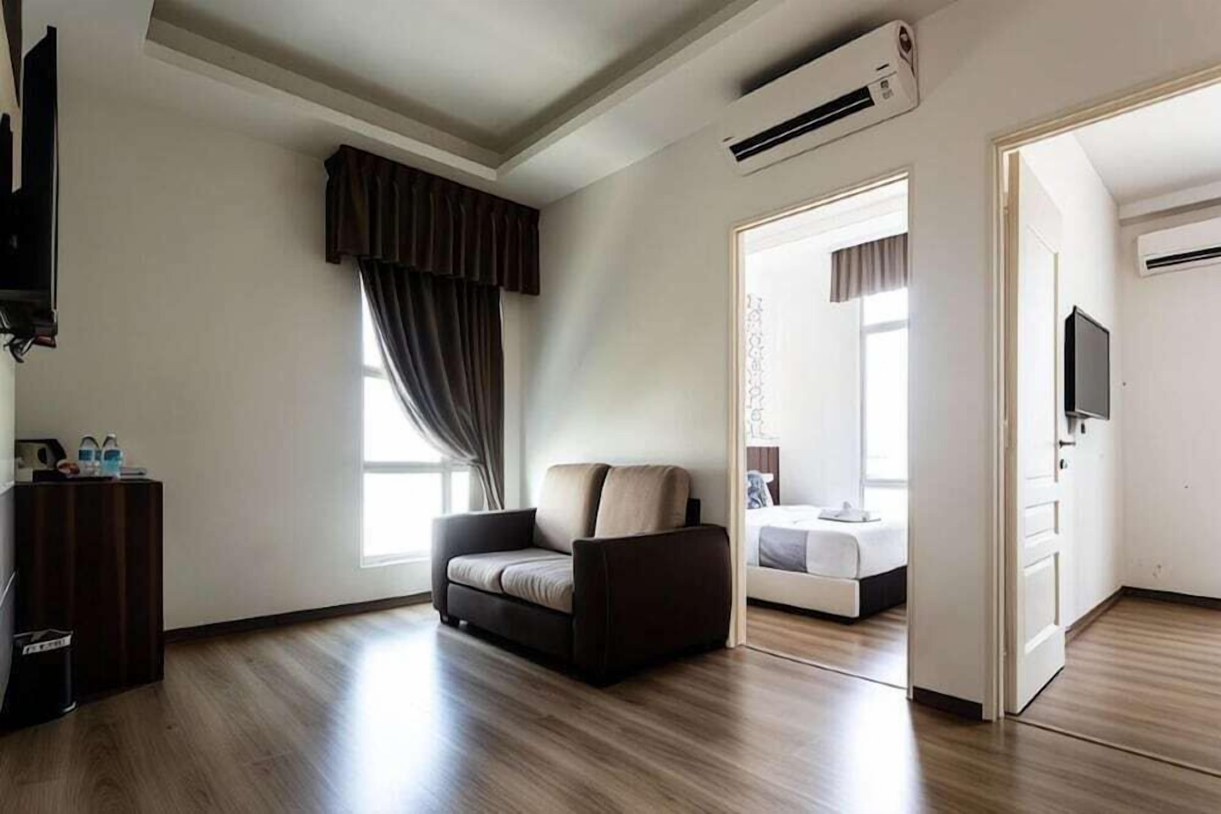 A modern hotel room with a sofa, a TV, an air conditioning unit, and a view of another room.