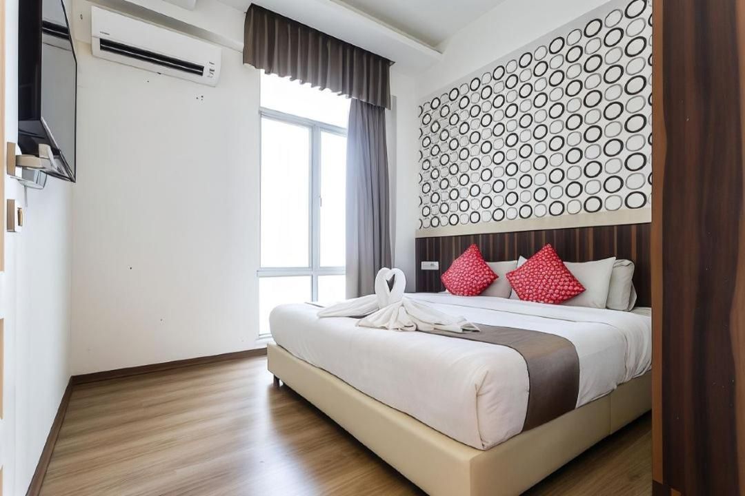 A hotel room with a bed, a wall-mounted air conditioner, a window with curtains, and a patterned wall.