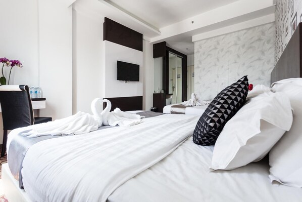 Una camera d'albergo con un letto, una televisione, uno specchio e un bagno visibile attraverso una porta aperta.