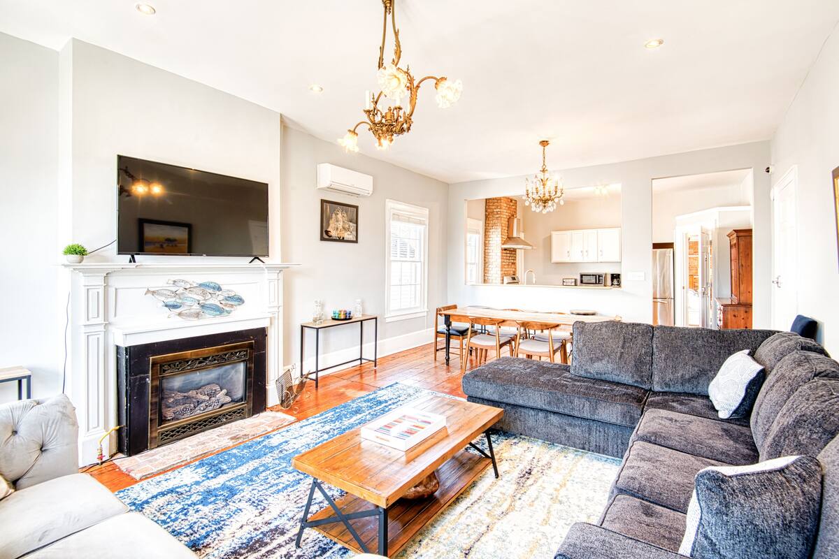 A spacious living room with a fireplace, a large sofa, a coffee table, and a chandelier.