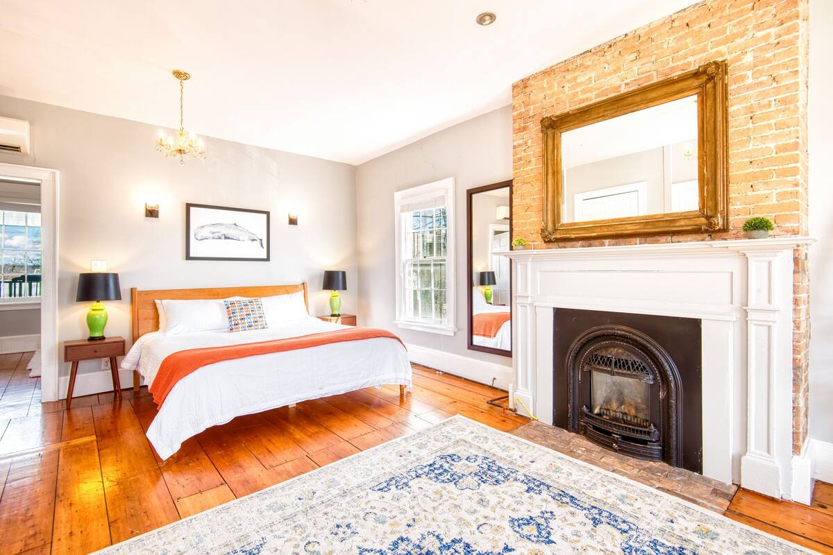 A bedroom with a bed, a fireplace, a mirror, and a chandelier.