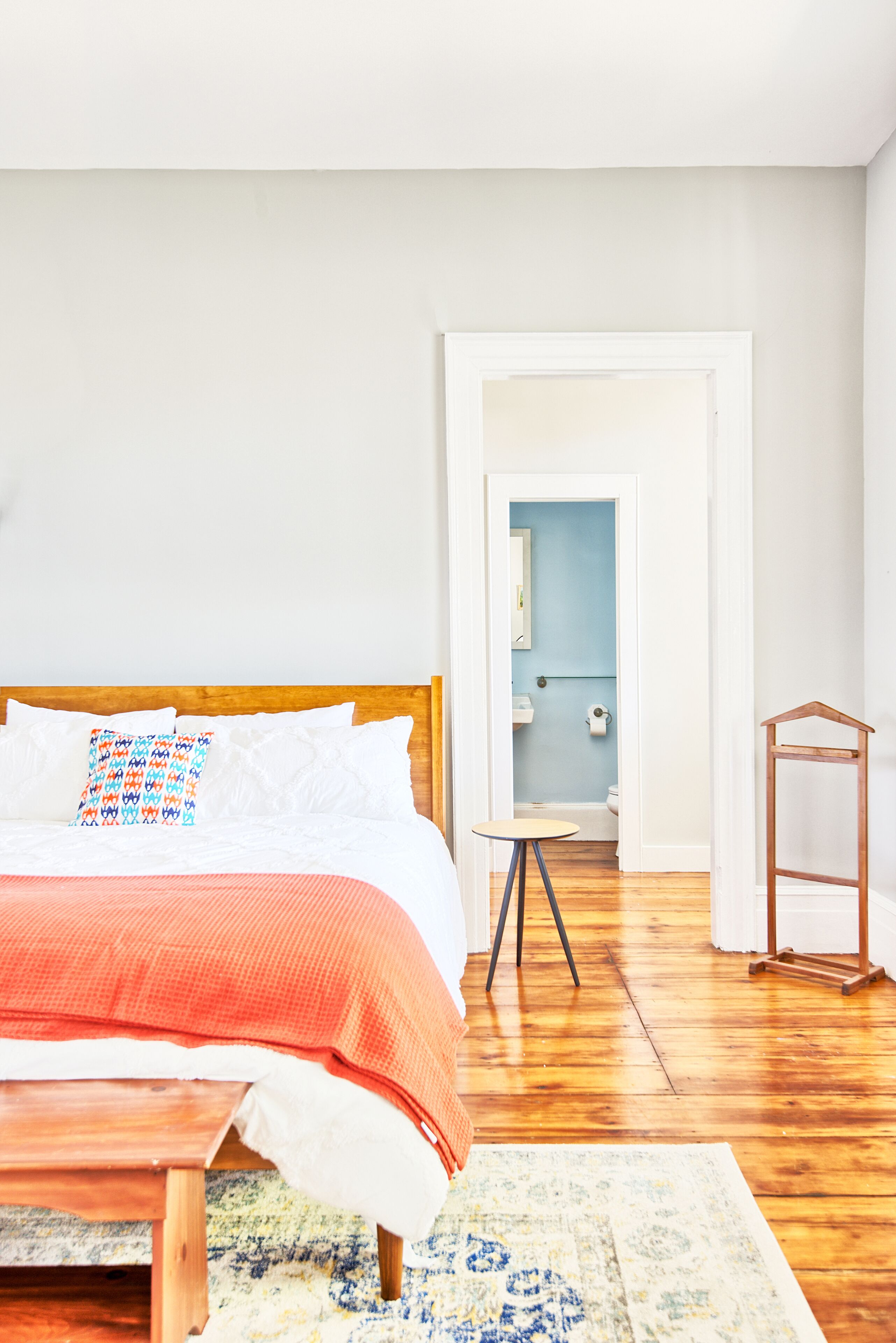 A bedroom with a wooden bed, a small bedside table, and a view into a bathroom.
