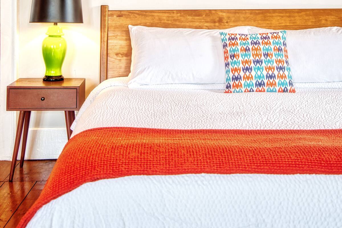 A neatly made bed with a colorful pillow, a framed whale artwork on the wall, and a lamp on a bedside table.